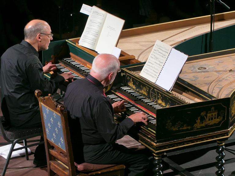 An zwei Cembali, die nebeneinander stehen, sitzen die beiden Musiker.