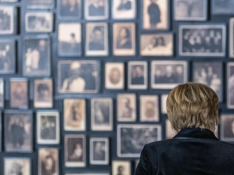 Eine Frau steht vor einer Wand mit vielen Bildern von Menschen.