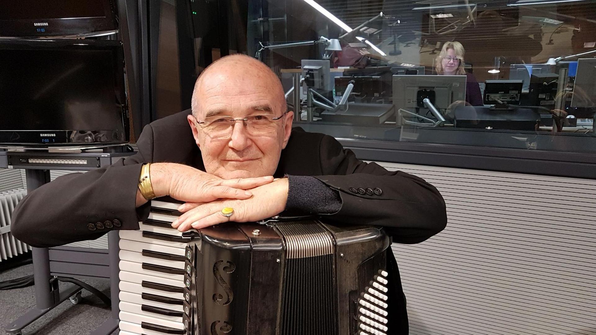 Stefan Sterzinger sitzt mit einem Akkordeon auf dem Schoß in einem Tonstudio, er stützt sich auf das Instrument und lächelt direkt in die Kamera.