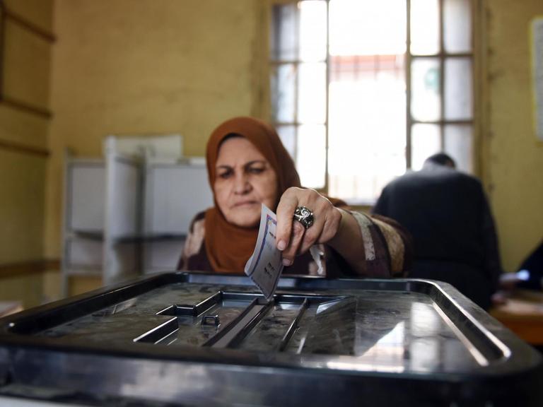 Eine Frau steckt ihren Wahlzettel für die Parlamentswahl in Ägypten in eine Wahlurne.