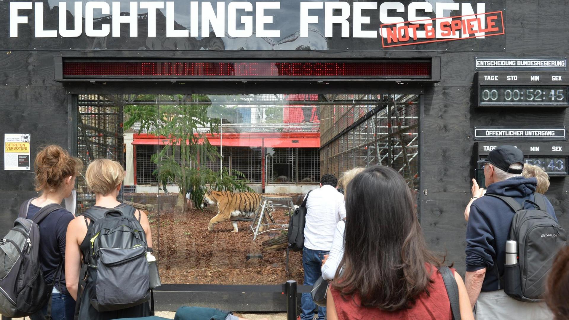  Menschen schauen in den Tiger-Käfig vor dem Theater. 