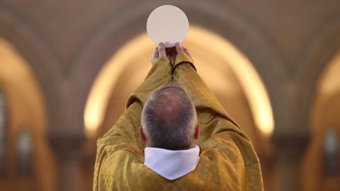 Ein katholischer Priester hält bei der Eucharistiefeier die Hostie hoch.