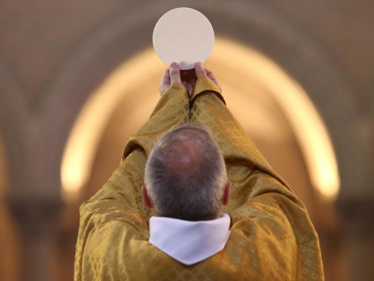 Ein katholischer Priester hält bei der Eucharistiefeier die Hostie hoch.