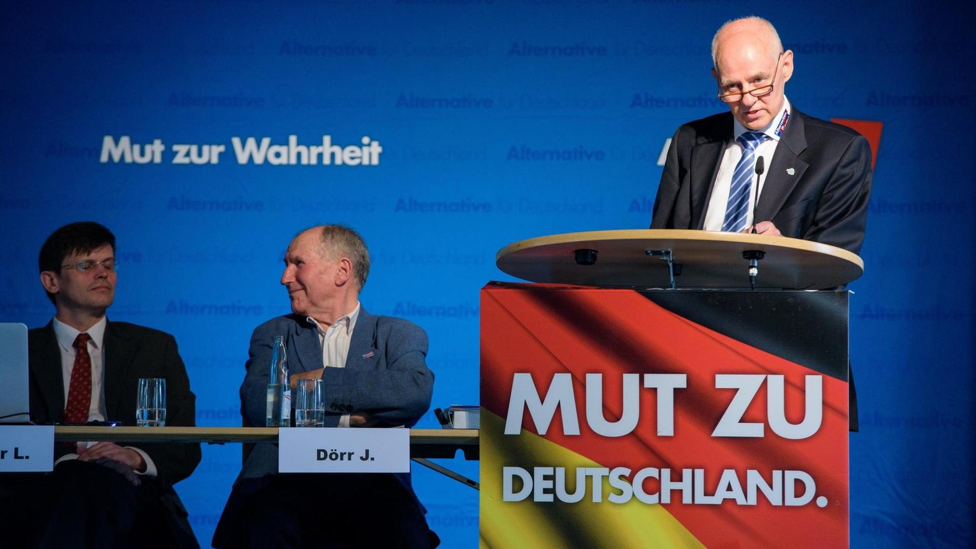 Rudolf Müller, AfD Saarland, spricht an einem Rednerpult. Links von ihm sitzen zwei Männer an einem Tisch.