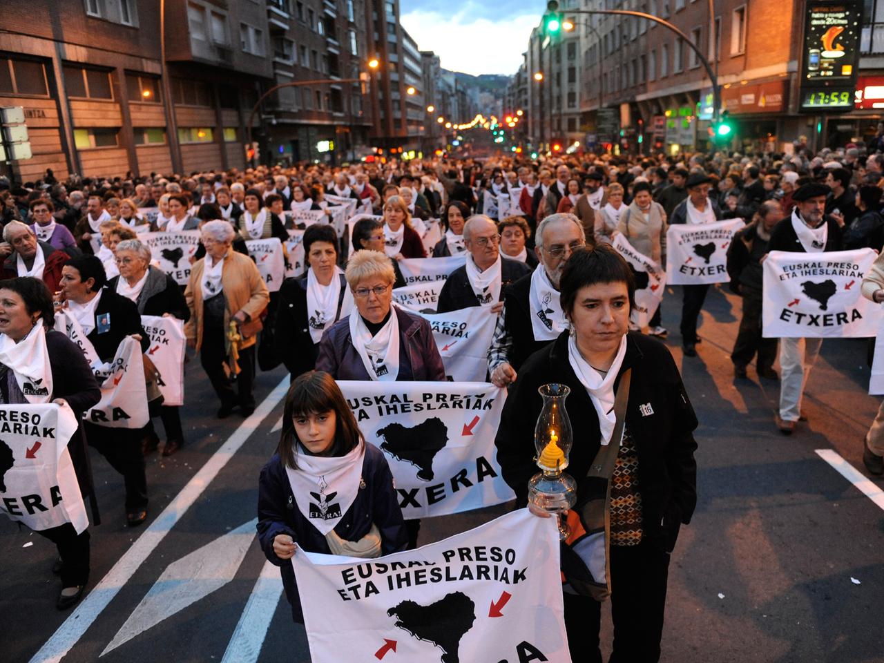 Demonstranten im Dunkeln auf einer Straße, die weiße Banner und Kerzen halten, auf den Bannern ist in baskisch zu lesen: "Mit allen Rechten. Baskische Häftlinge zurück ins Baskenland."