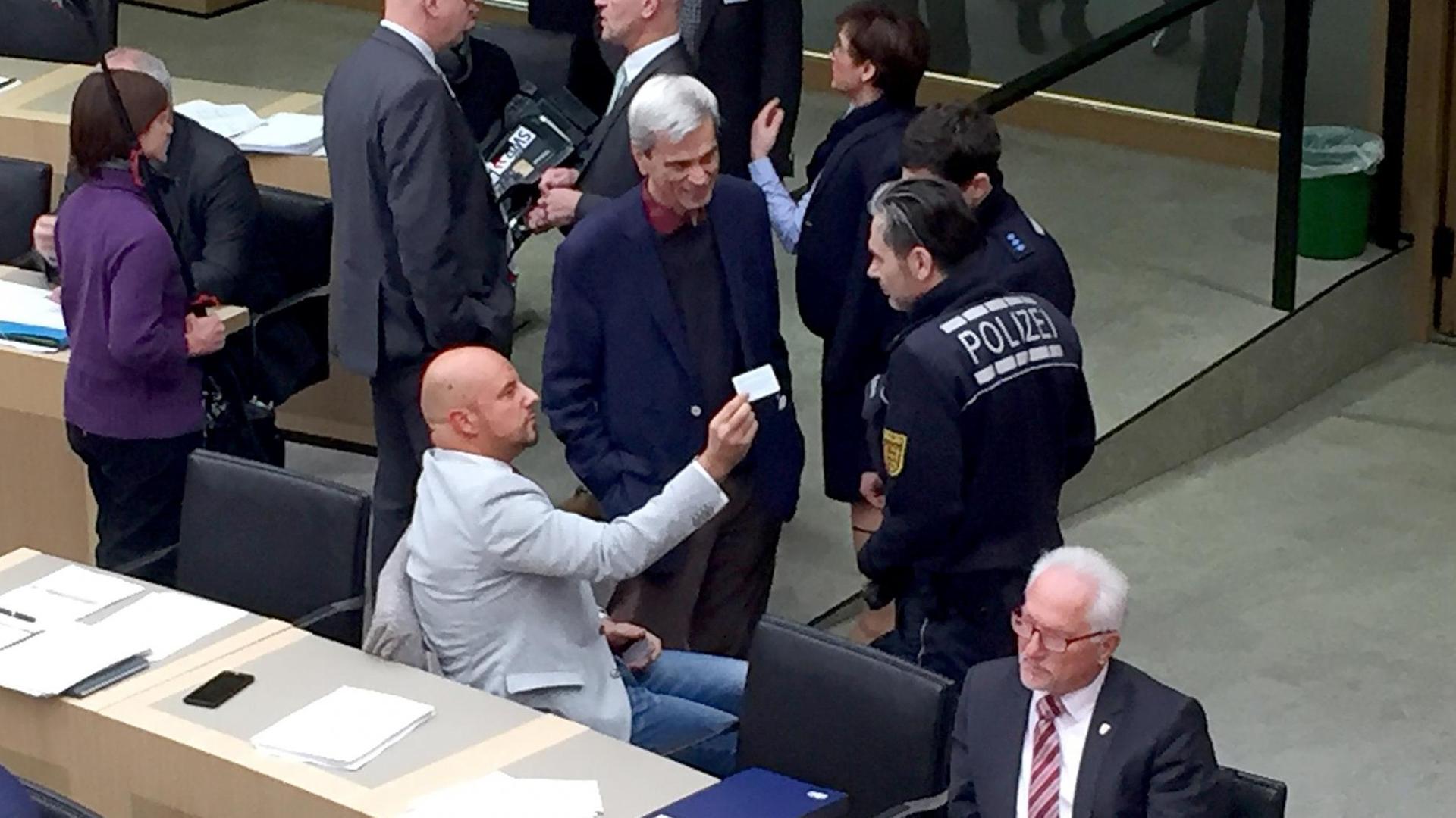 12.12.2018, Baden-Württemberg, Stuttgart: Stefan Räpple (sitzend, l), Abgeordneter der AfD im Landtag von Baden-Württemberg, spricht während einer Plenarsitzung mit Polizisten. Zuvor hatte er sich geweigert, trotz Aufforderung der Landtagspräsidentin, den Saal zu verlassen. In der Mitte steht der fraktionslose Landtagsabgeordnete und AfD-Politiker, Wolfgang Gedeon, (zu dpa: "Polizei-Einsatz im Plenum - Landtagssitzung wegen Räpple unterbrochen" vom 12.12.2018) - Bestmögliche Qualität - Foto: Nico Pointner/dpa | Verwendung weltweit