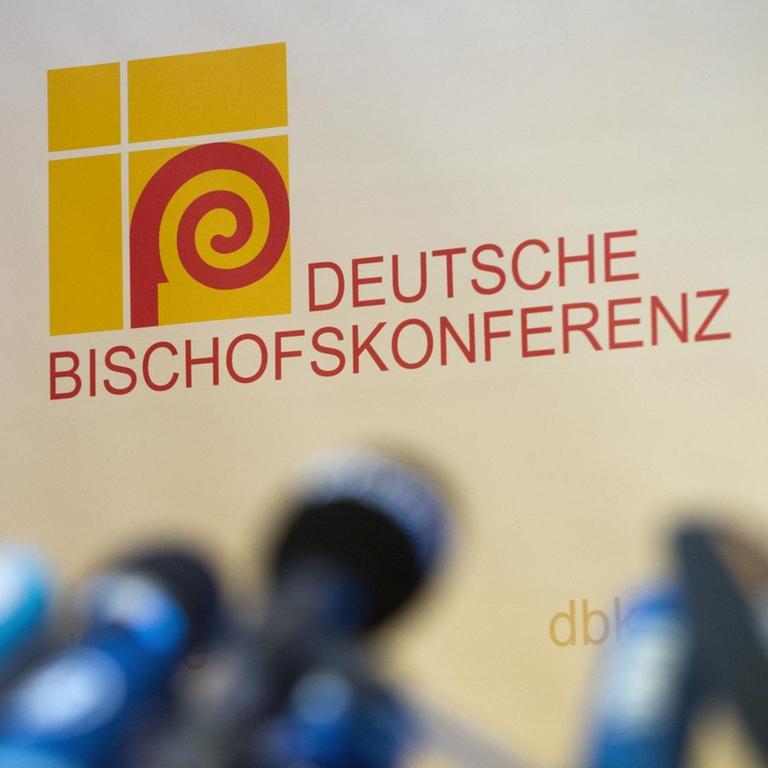 Presse-Mikrofone stehen unscharf abgelichtet vor dem Logo der Deutschen Bischofskonferenz