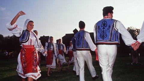 Hand in Hand tanzende Frauen und Männer in traditionell bestickten Kleindern und Westen.