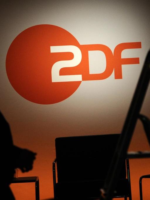 Ein Techniker steht neben einer Leiter vor einem ZDF-Logo. Auf einem Tisch sieht man Mineralwasser und Gläser.