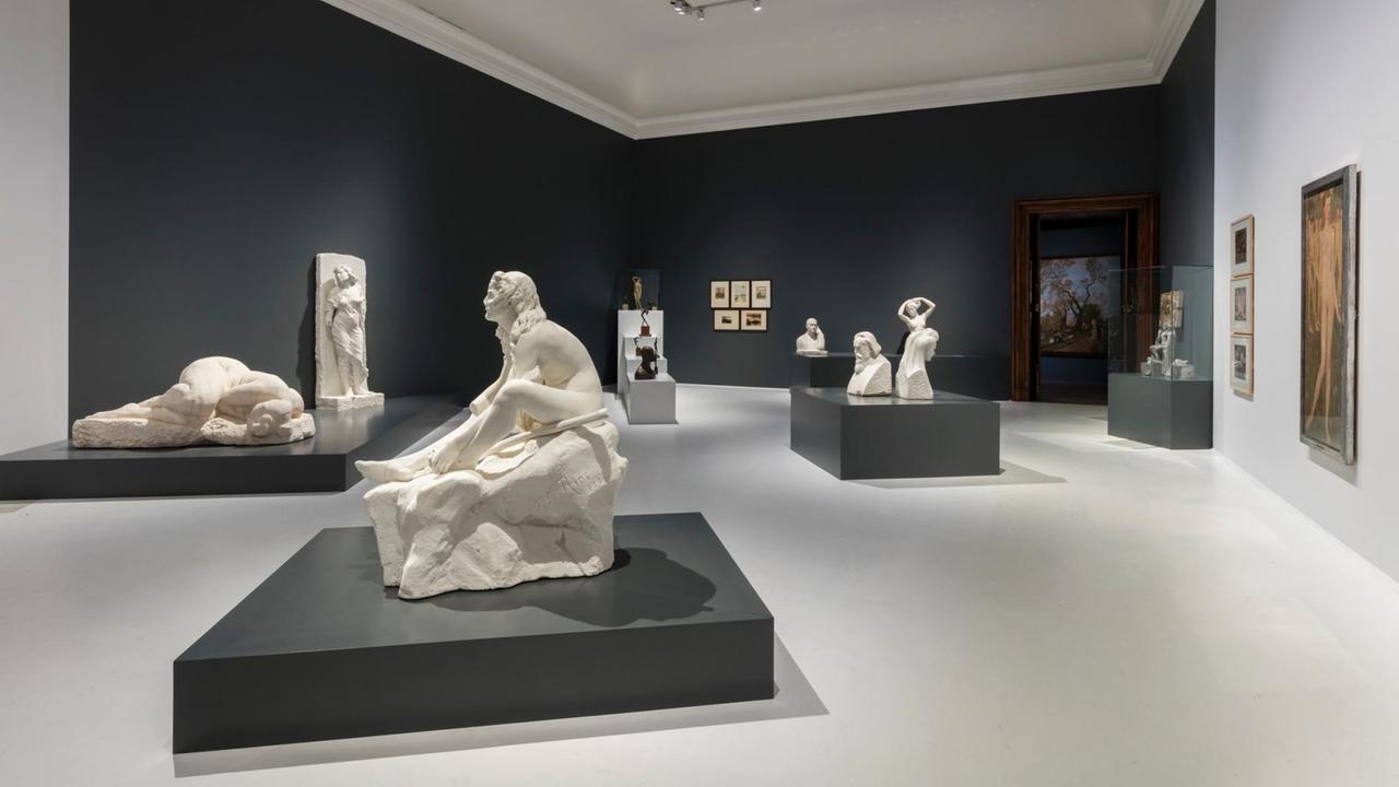 Blick in einen Ausstellungsraum der mit Skulpturen und Gemälden bestückt ist.