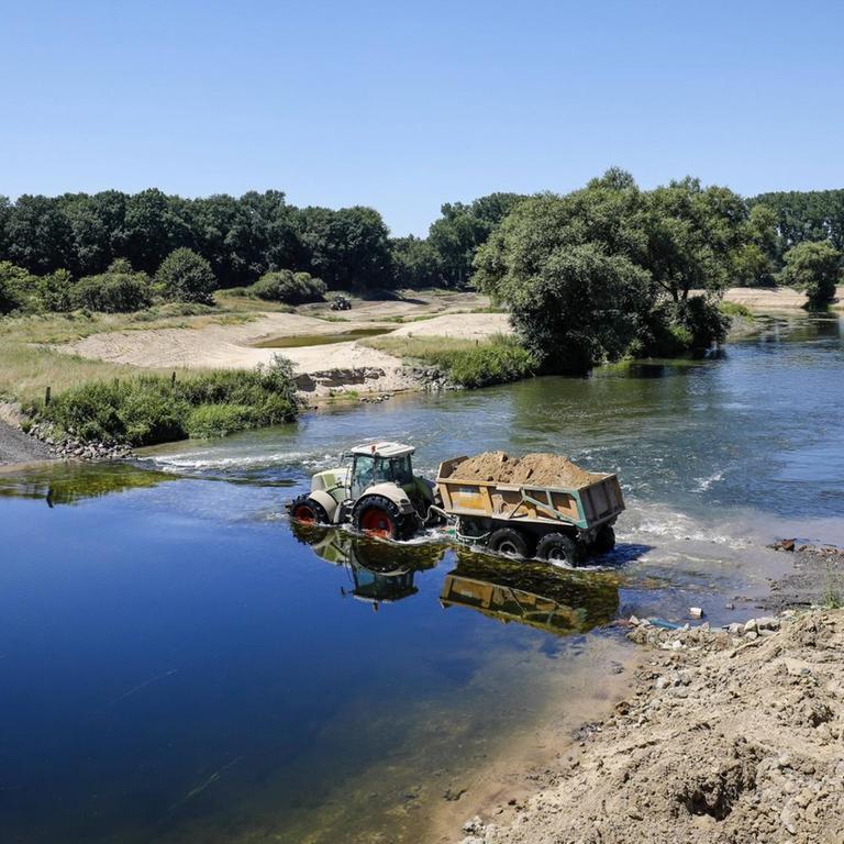 Ein Trecker mit einem Anhänger voller Sand durchquert den Fluss Lippe. Hier wird eine naturnahe Flusslandschaft geschaffen, ein intaktes Fluss-Auen-Ökosystem wiederhergestellt.