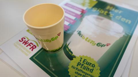 Ein Mehrwegbecher aus Kunststoff steht am 21.11.2016 in Freiburg (Baden-Württemberg) in der Unibibliothek auf einem Werbeplakat.