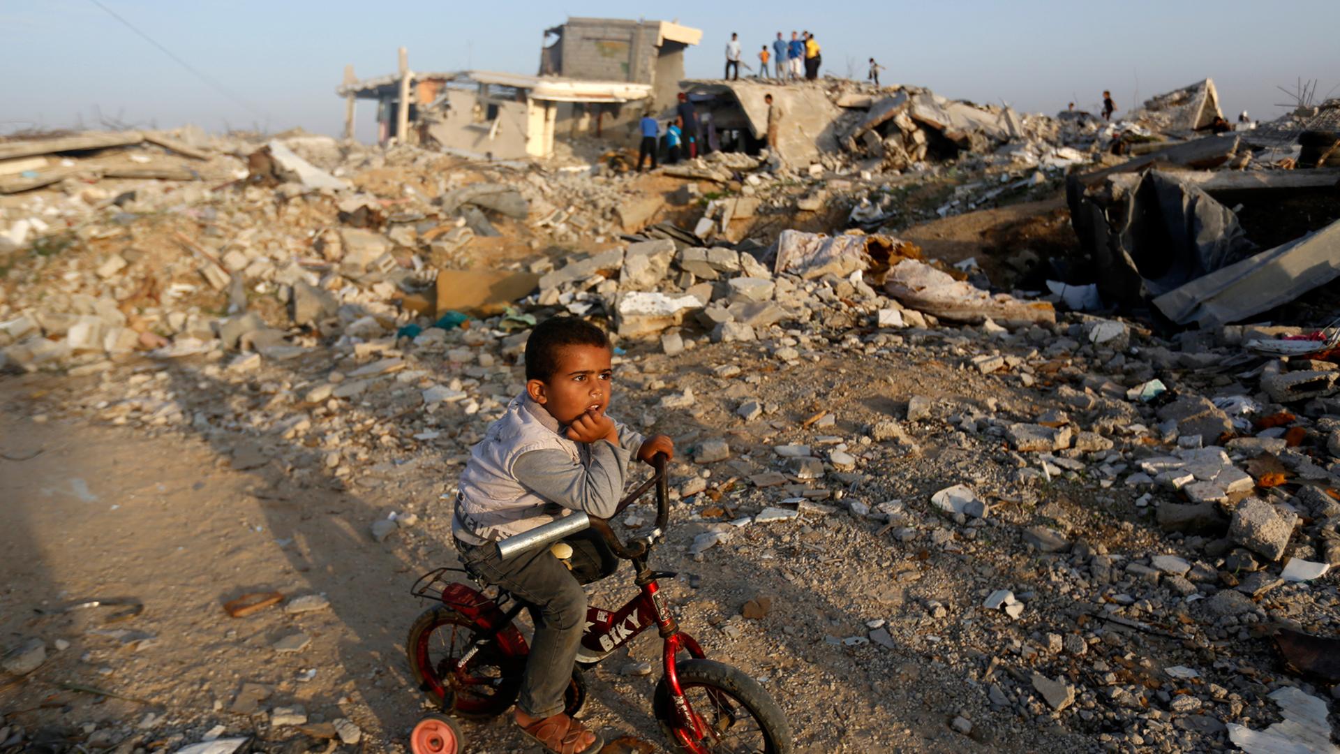 Ein Junge sitzt auf seinem Fahrrad im Gazastreifen inmitten von zerstörten Gebäuden.