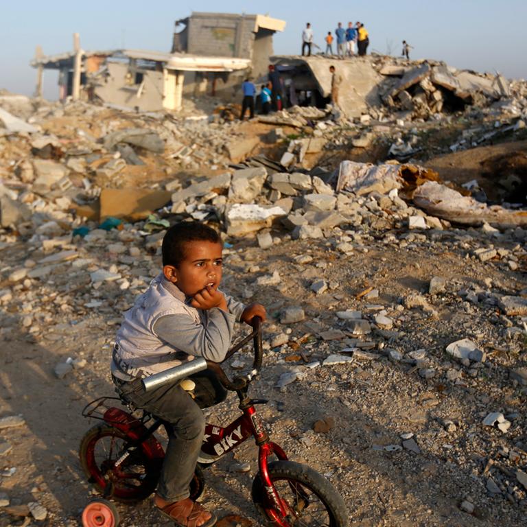 Ein Junge sitzt auf seinem Fahrrad im Gazastreifen inmitten von zerstörten Gebäuden.