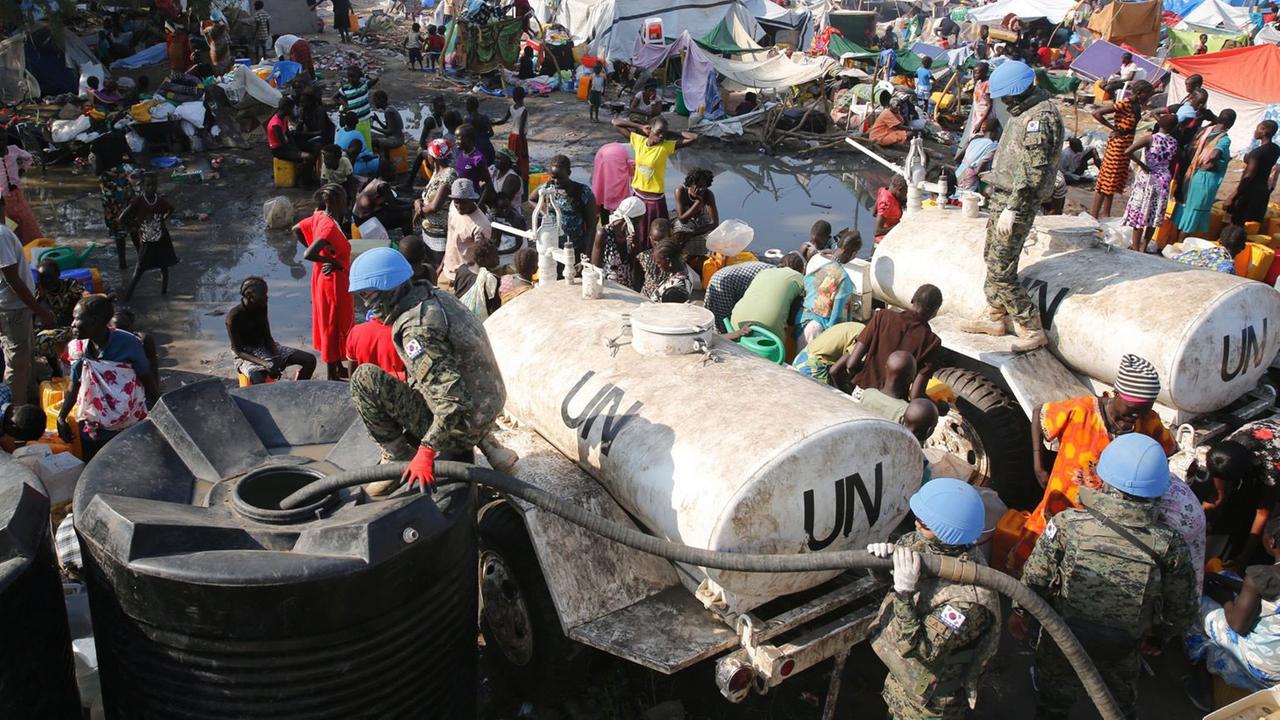 Südkoreanische UNO-Soldaten verteilen Wasser an ein Flüchtlingslager im Südsudan, das aus vielen Zelten und Hunderten Menschen besteht.