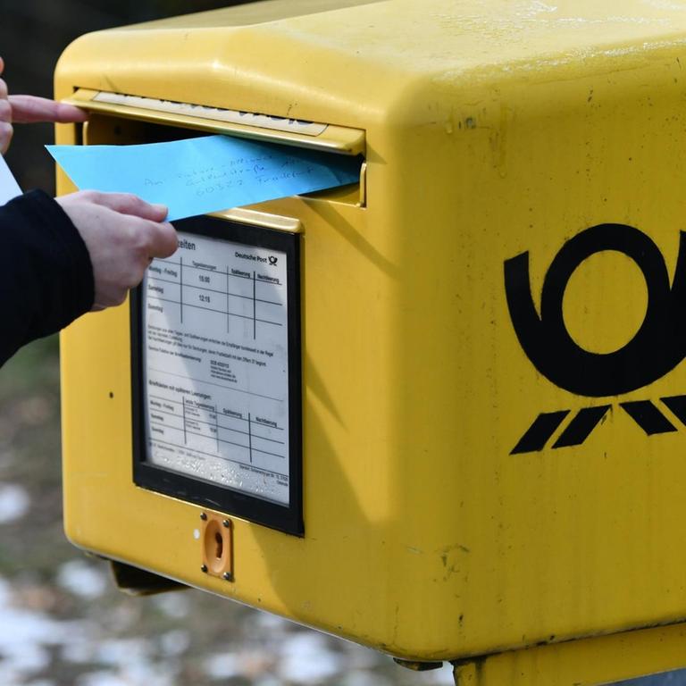 Eine Frau wirft Briefe in einen Briefkasten ein.