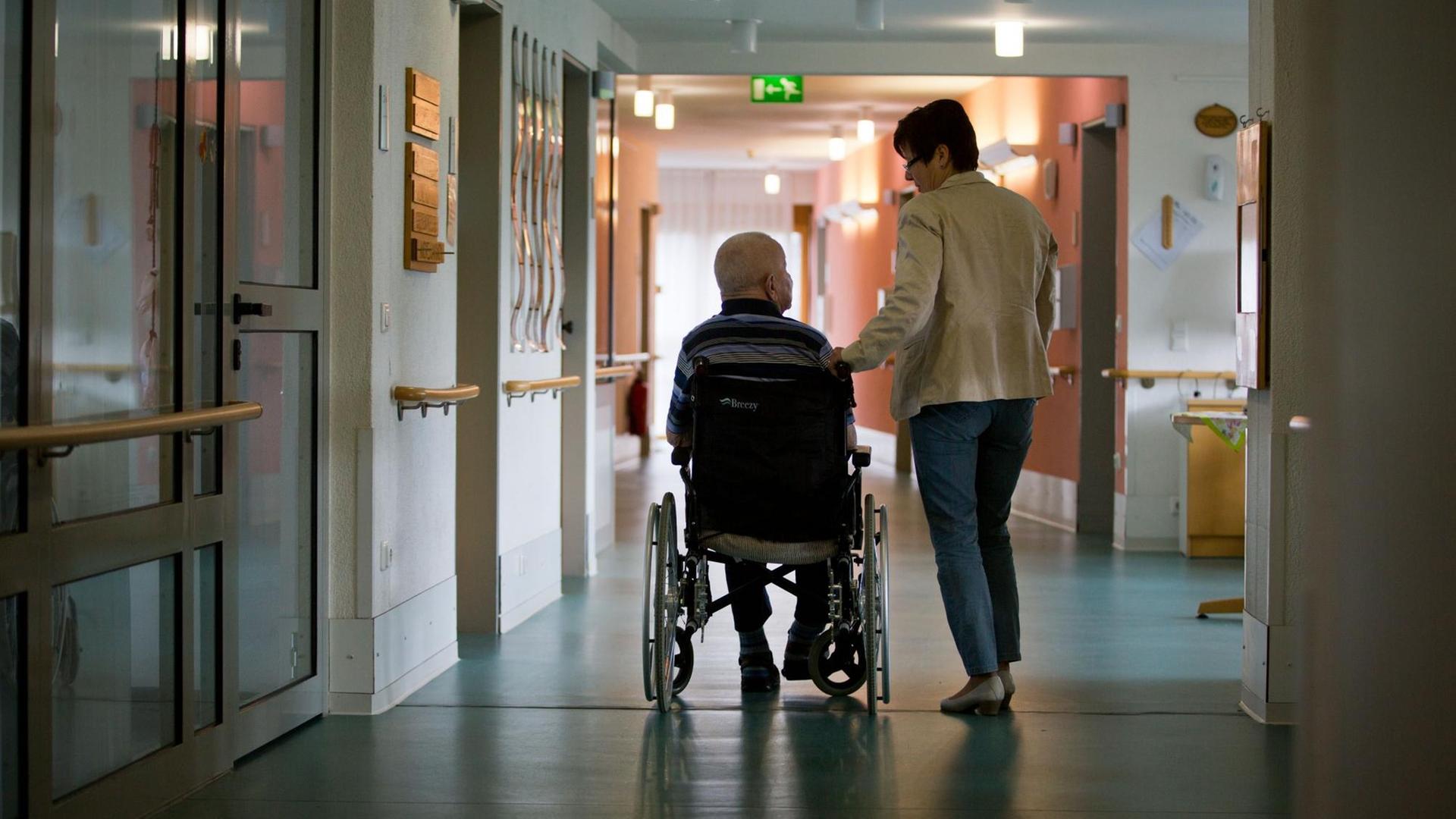 Eine Frau mit einem Mann in einem Rollstuhl in einem Gang eines Pflegeheims.