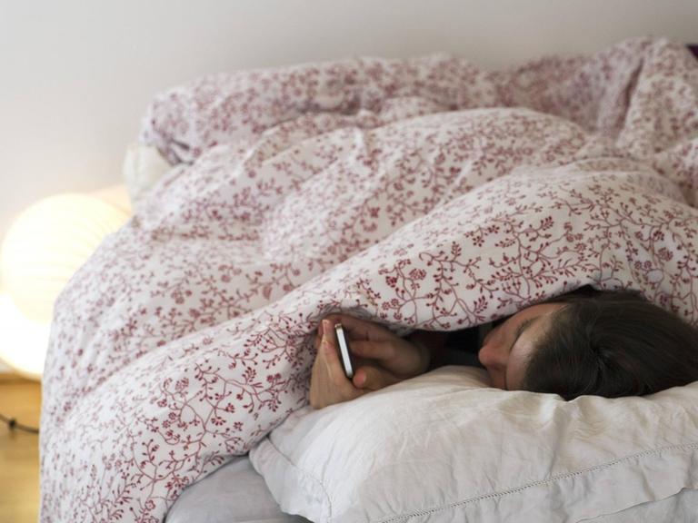 Eine Frau liegt im Bett und blickt auf ihr Mobiltelefon. Die Kommunikation über eine App soll in Zukunft bei Depressionen Lösungsansätze bieten.