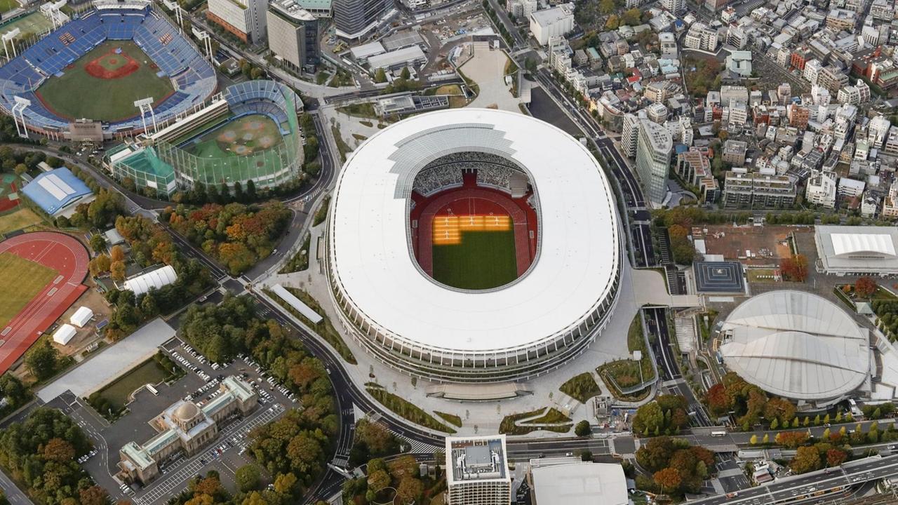 Luftaufnahme des Stadions in Tokio, im Innenraum ist ein Teil des Bodens hell erleuchtet.
