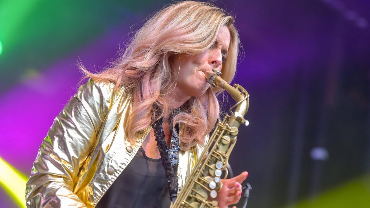 Eine Frau in goldener Jacke spielt Saxofon.