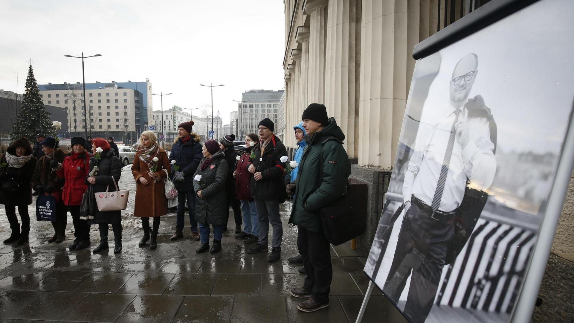 Ein Dutzend Demonstranten stehen in einer Grupper zusammen vor dem Sitz des Staatssenders TVP. Im Vordergrund ist ein groß ausgedrucktes Bild des ermordeten Danziger Bürgermeister Pawel Adamowicz zu sehen.