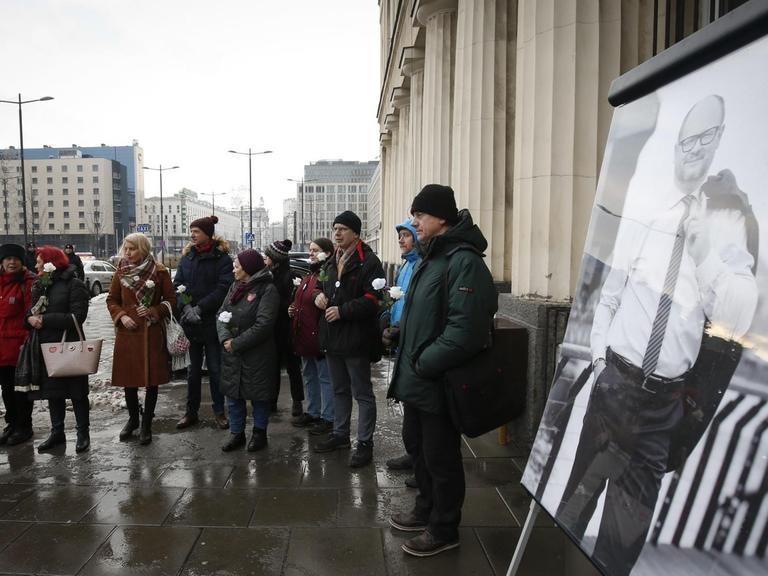 Ein Dutzend Demonstranten stehen in einer Grupper zusammen vor dem Sitz des Staatssenders TVP. Im Vordergrund ist ein groß ausgedrucktes Bild des ermordeten Danziger Bürgermeister Pawel Adamowicz zu sehen.