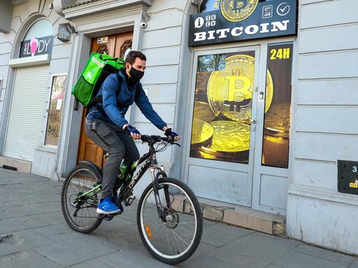 Ein Radfahrer mit Mundschutz fährt an einem Bitcoin-Wechsel-Laden in Krakau vorbei.