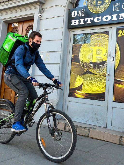 Ein Radfahrer mit Mundschutz fährt an einem Bitcoin-Wechsel-Laden in Krakau vorbei.