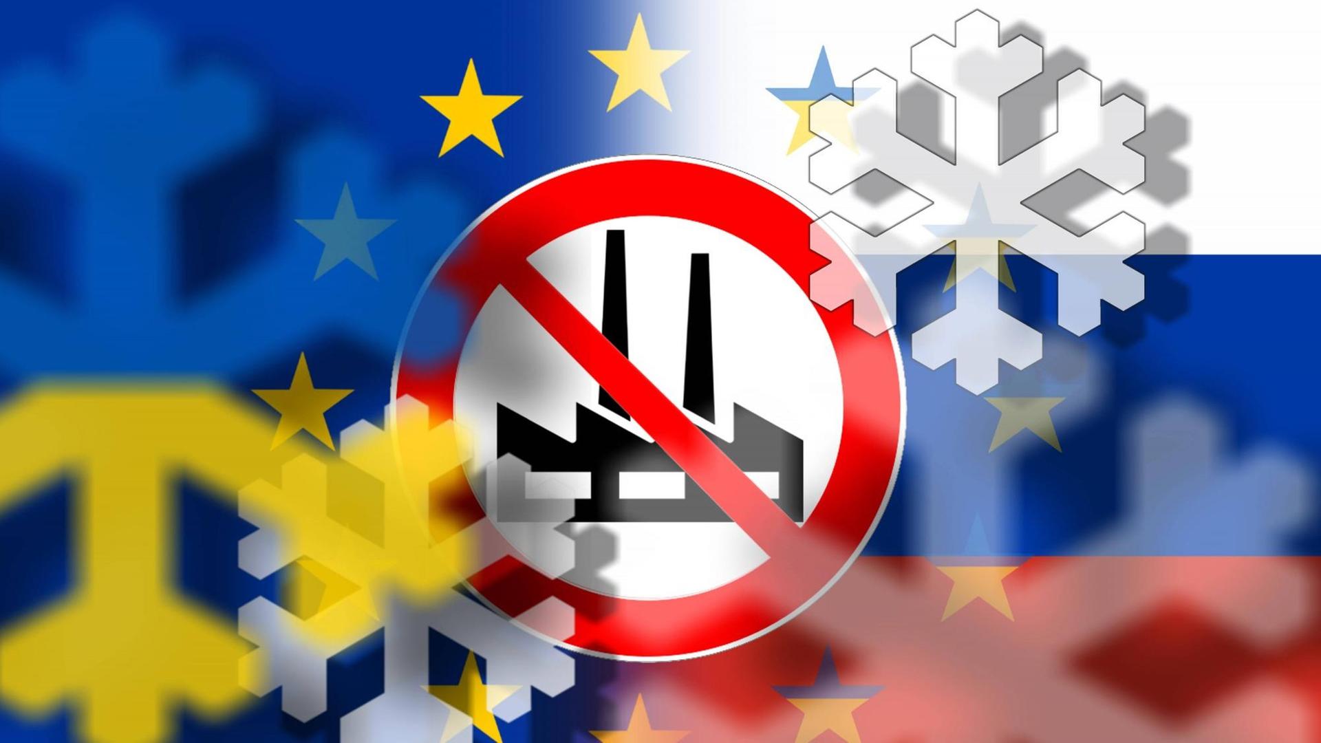 Symbolbild zu schärferen Wirtschaftssanktionen der EU gegen Russland: fiktives Verkehrsschild mit durchgestrichener Industrieanlage vor Flaggen der EU, Russland sowie der Ukraine und Symbolen von Eiskristallen und Schneeflocken