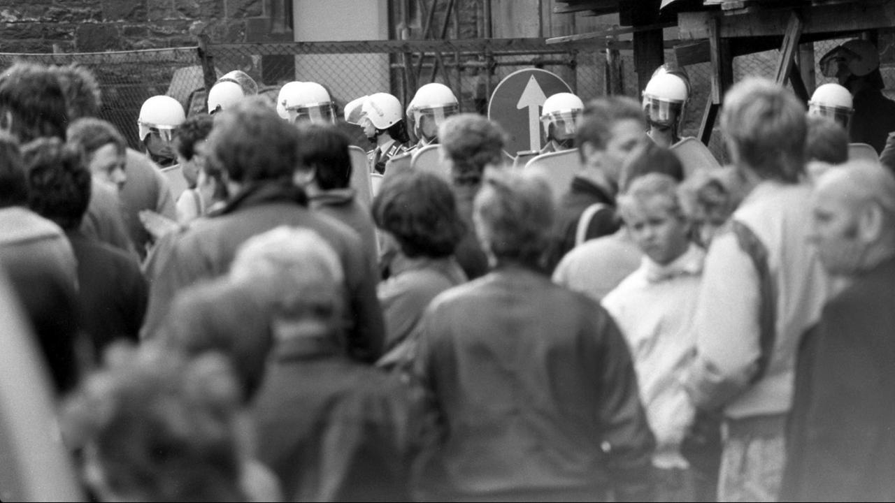 Am Sonnabend, dem 7. Oktober 1989 - dem Nationalfeiertag zur Gründung der DDR - und zwei Tage vor der historischen Montagsdemonstration mit über 70.000 Teilnehmern auf dem Karl-Marx-Platz stehen Bürgerinnen und Bürger von Leipzig ganz ruhig auf dem Nikolaikirchhof vor der Nikolaikirche in Leipzig zusammen, der von Polizisten in alle Himmelsrichtungen abgeriegelt ist.