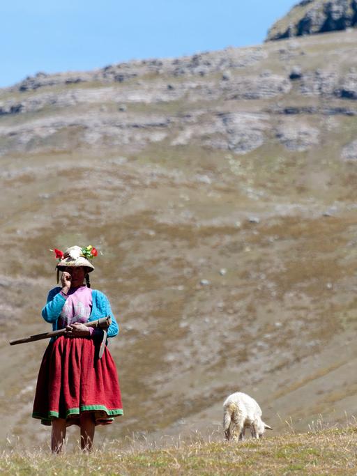 Eine Frau in traditioneller Kleidung steht vor einem Berpanorama in den peruanischen Anden.