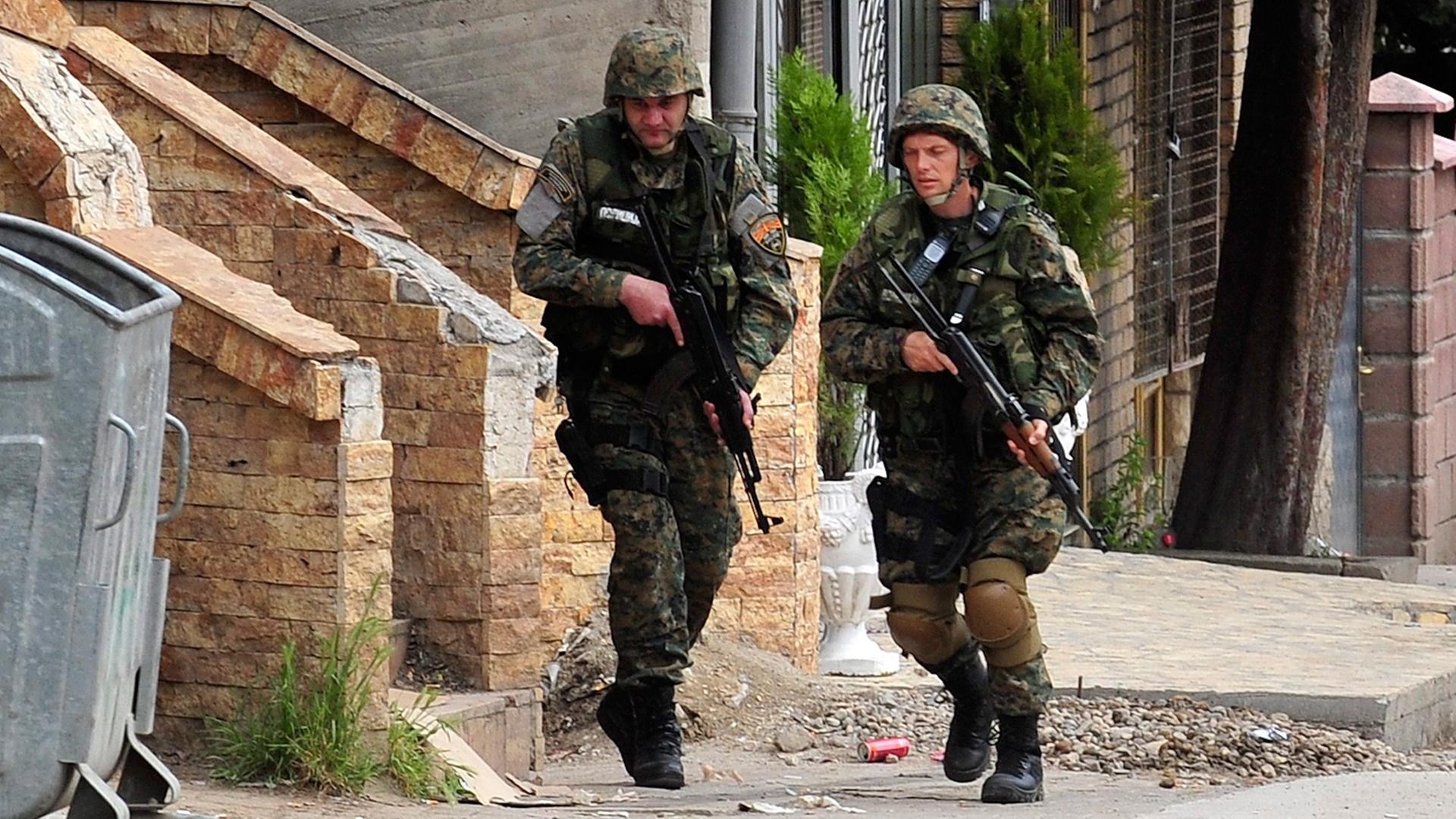 Zwei mit Gewehren bewaffnete mazedonische Polizisten laufen durch eine Straße von Kumanovo.