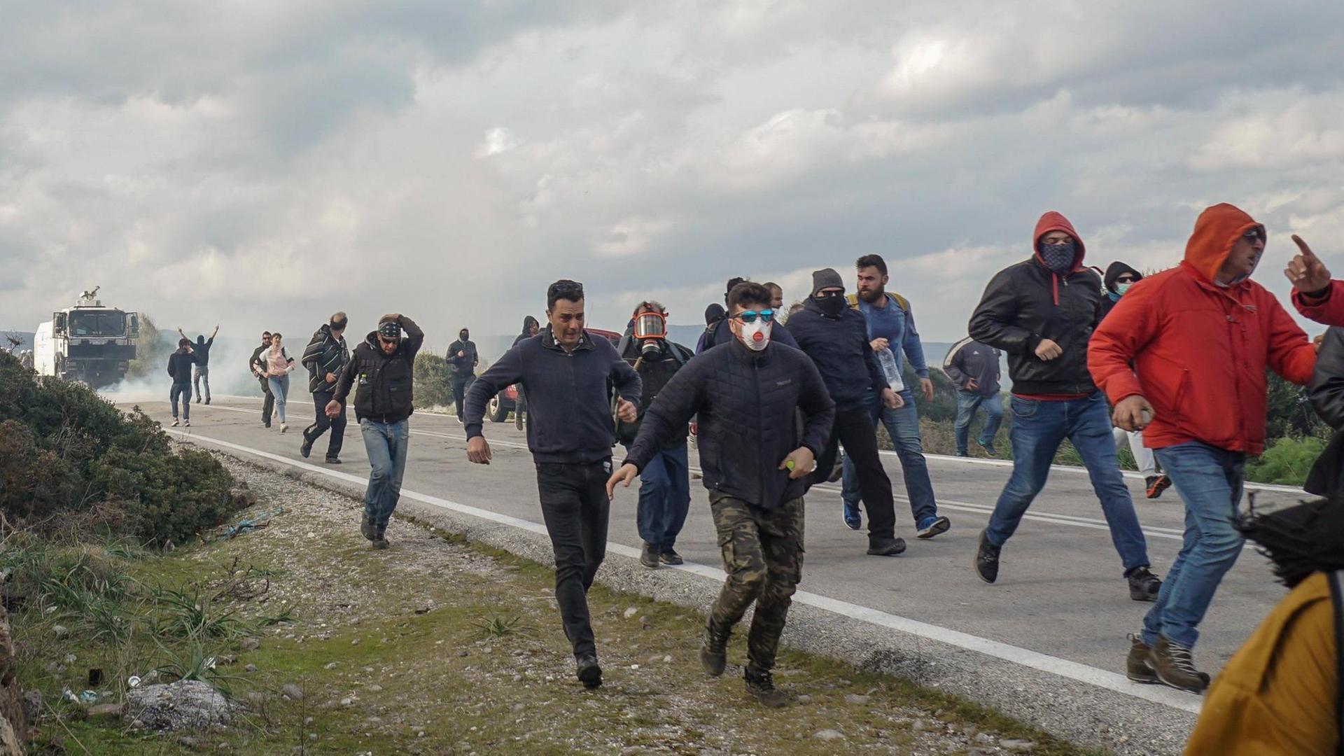Demonstrierende rennen auf der Insel Lesobos eine Straße entlang, nachdem die Polizei Tränengas eingesetzt hat.
