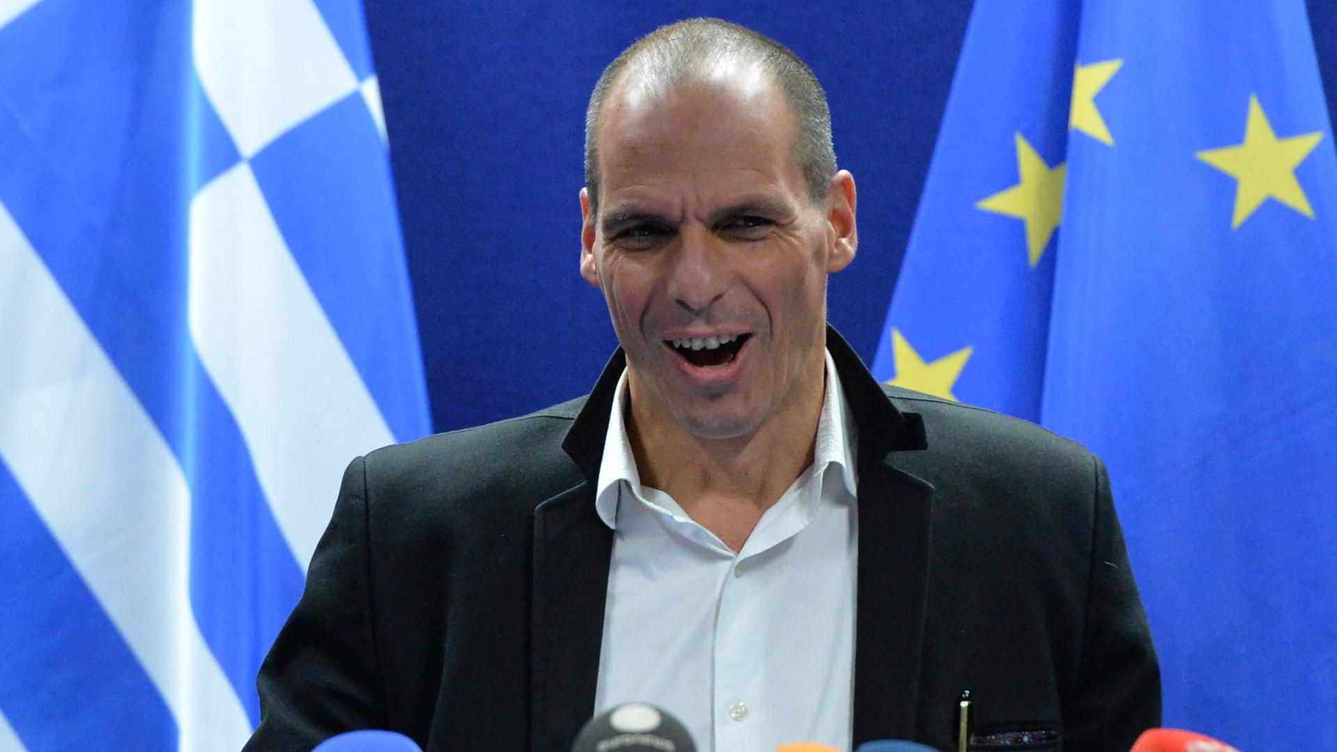 Der griechische Finanzminister Yannis Varoufakis steht hinter einigen Mikrofonen und verzerrt das Gesicht.