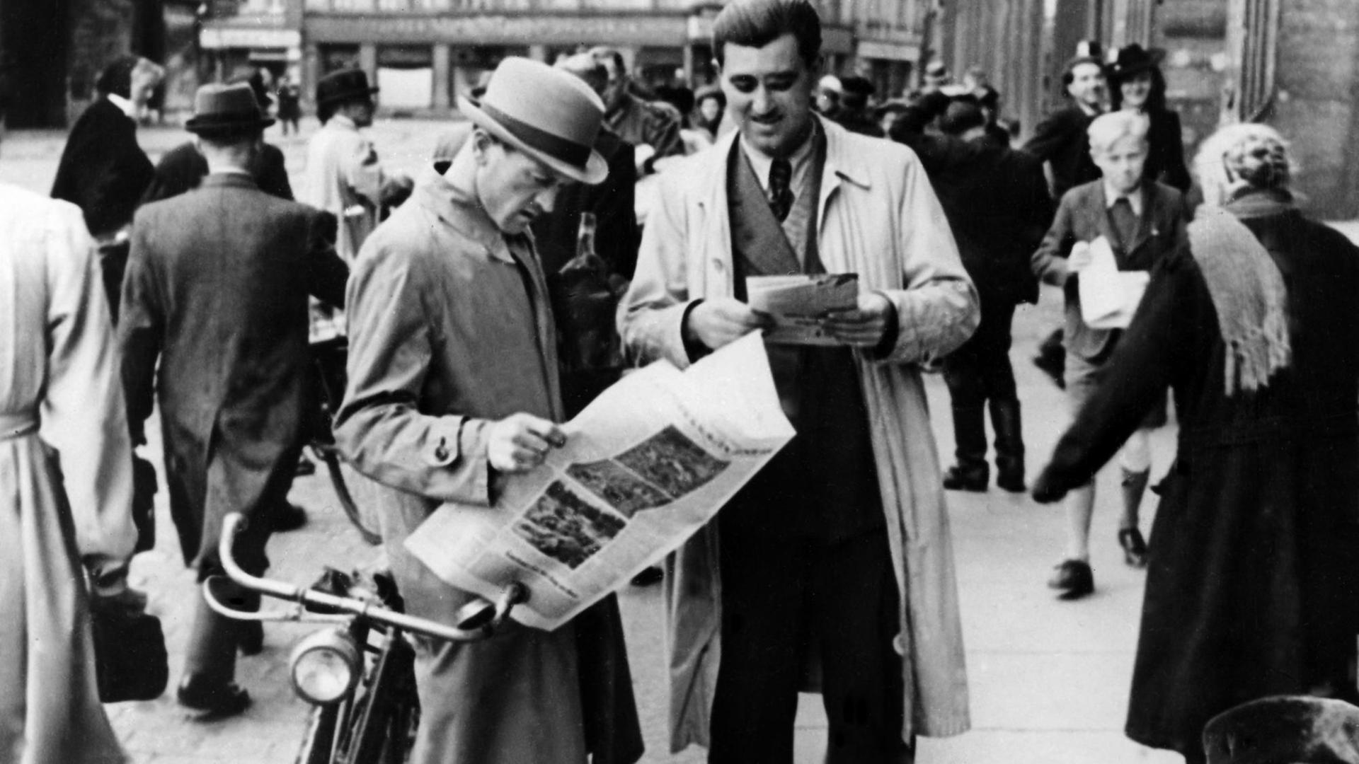 Das schwarz-weiß Foto zeigt zwei Männer, die die "Aachener Nachrichten" lesen, die als erste deutsche Zeitung nach dem Zweiten Weltkrieg erschien