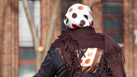 Eine Frau mit Kopftuch steht an einer Straße