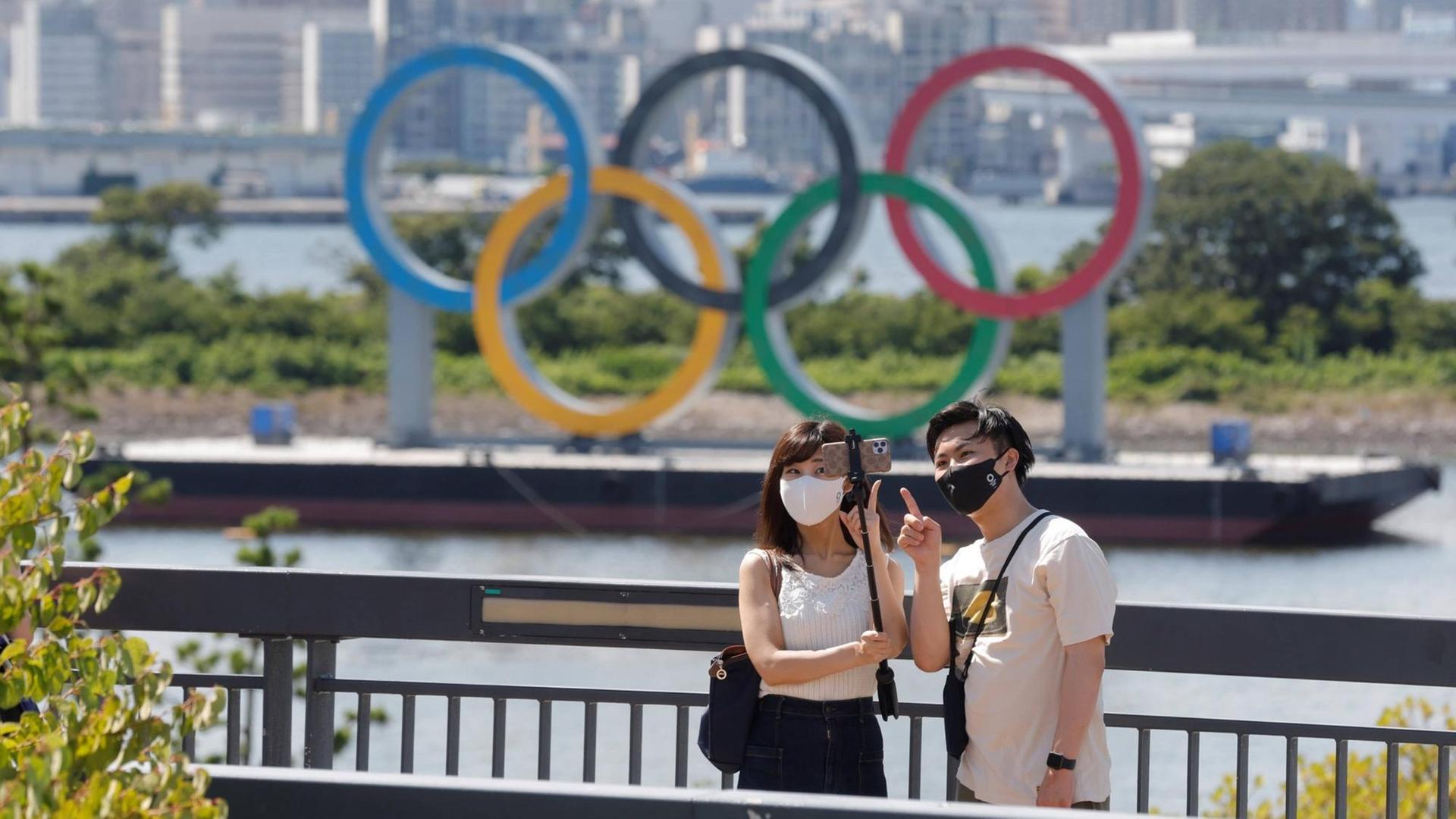 Ein paar macht ein Foto vor den Olympischen Ringen in Tokio.