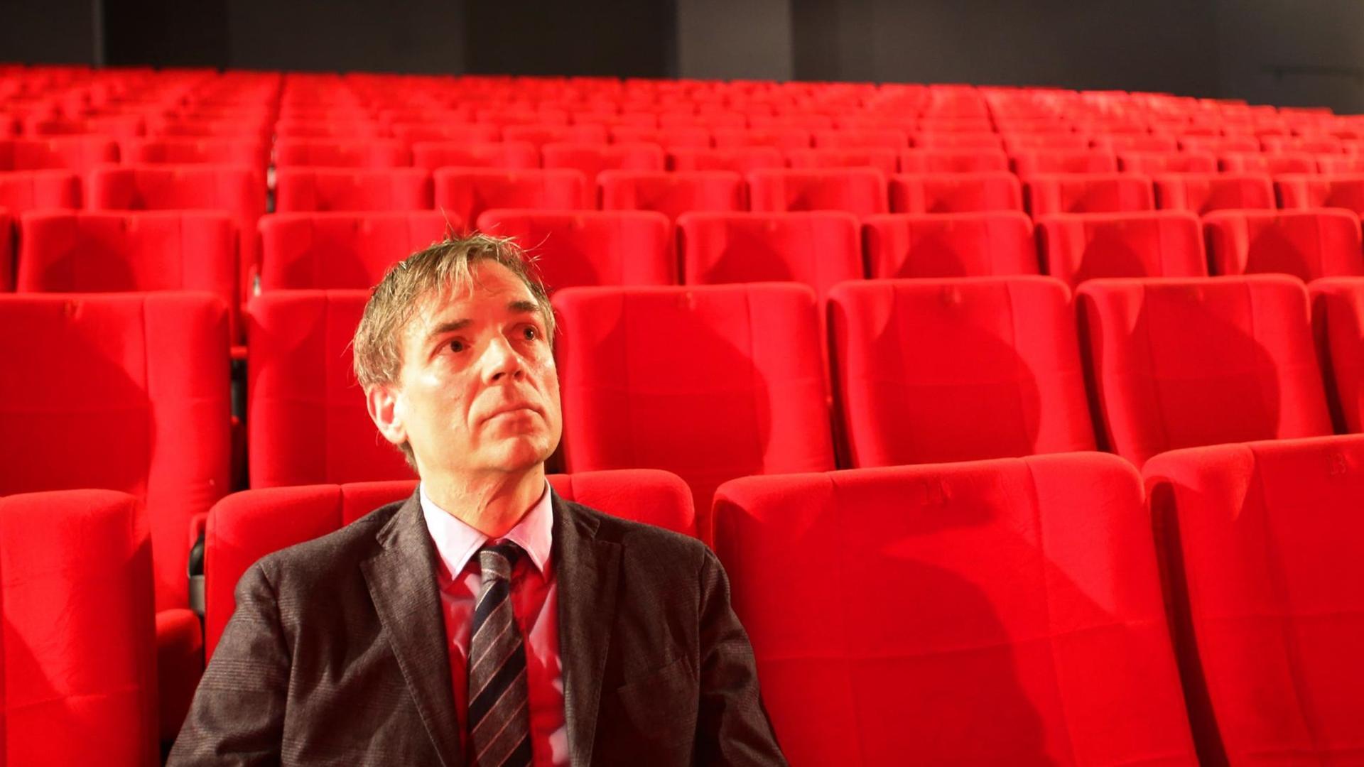 Lars Henrik Gass sitzt alleine in einem Kinosaal mit roten Sitzen