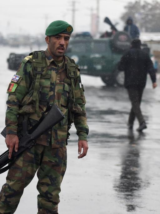 Ein uniformierter Soldat mit Maschinengewehr läuft über die Straße, im Hintergrund weitere Soldaten und Militärfahrzeuge.