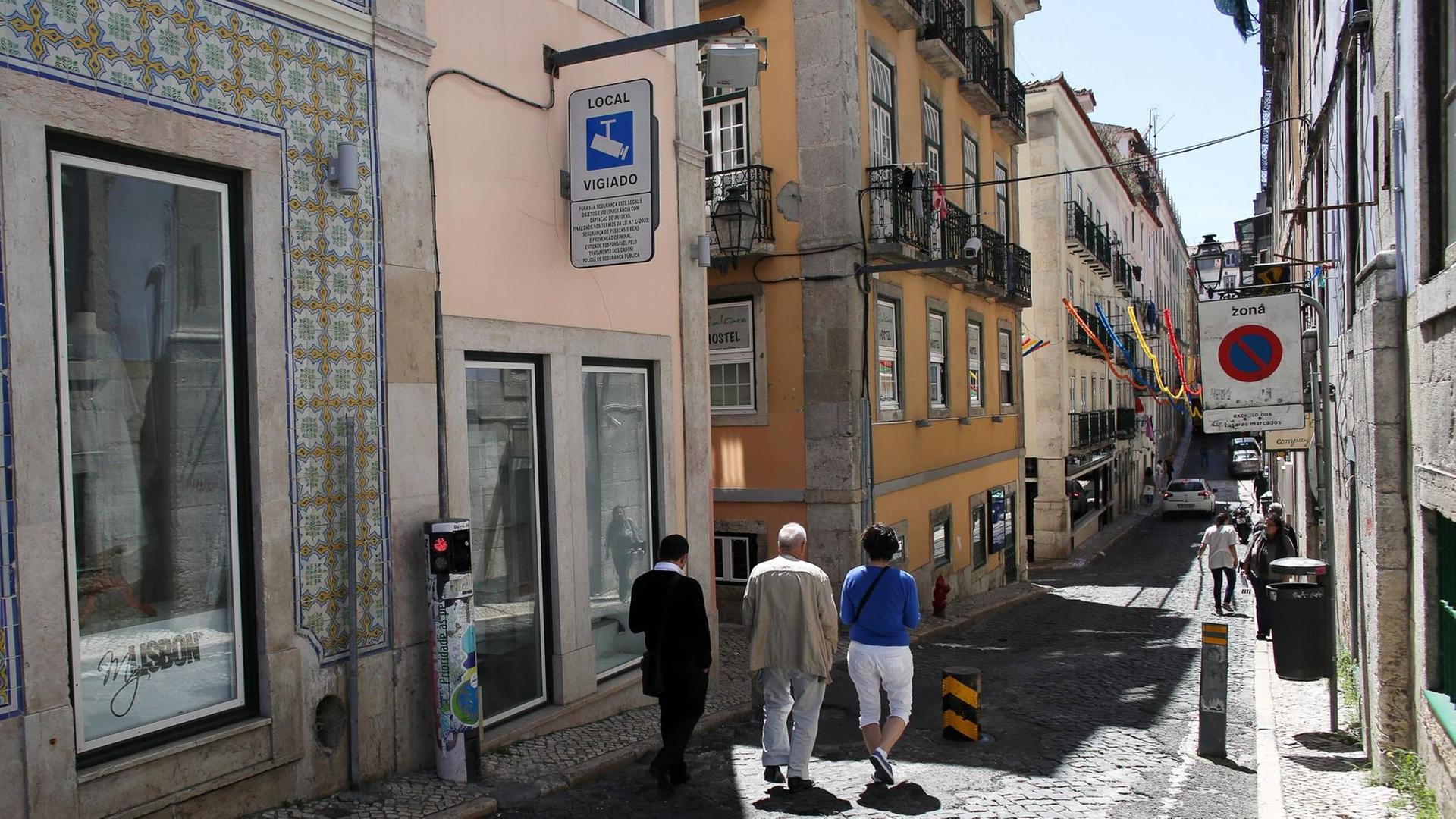 Eine schmale Straße im Bairro Alto, der Oberstadt von Lissabon. Links hängt ein Straßenschild mit dem Kamera-Logo und der Aufschrift 'Local Vigiado'