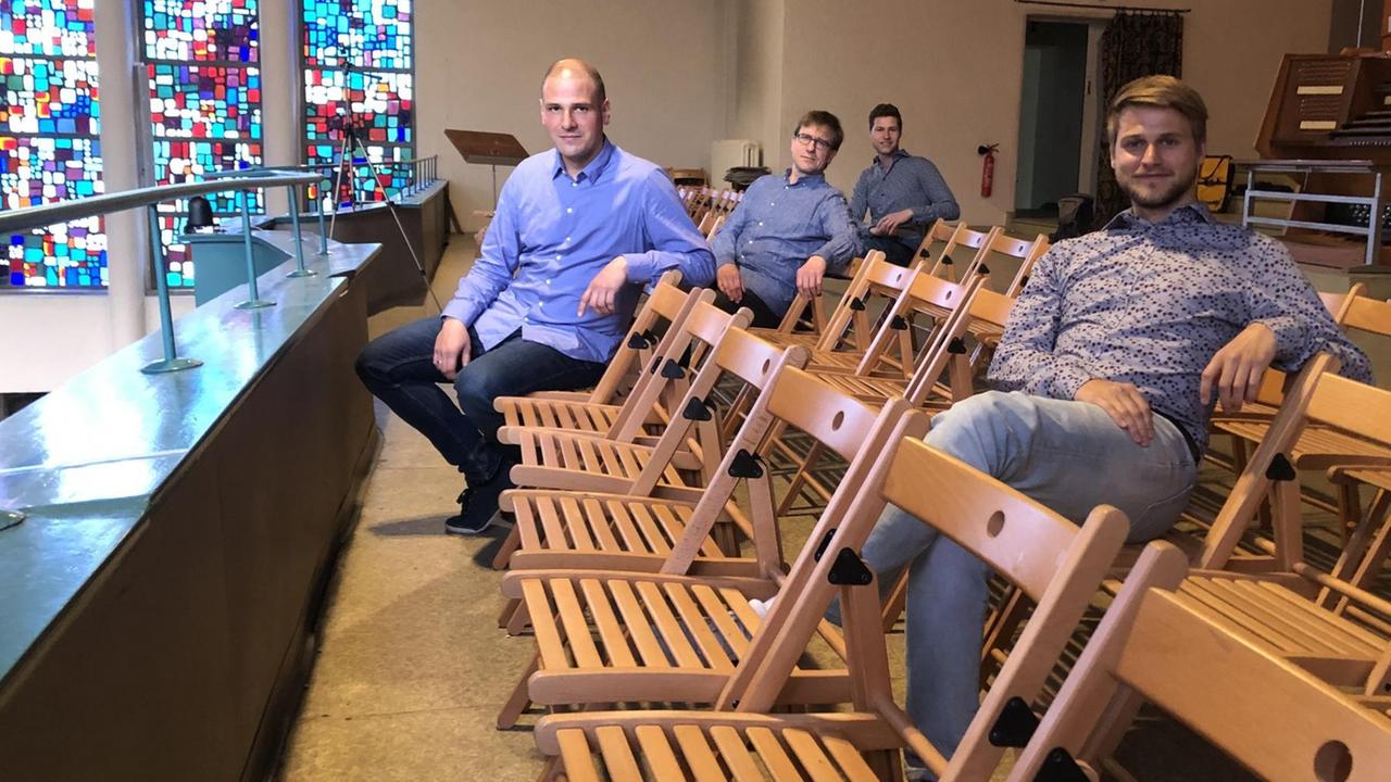 Vier junge Männer sitzen verteilt auf der Empore der Kirche.