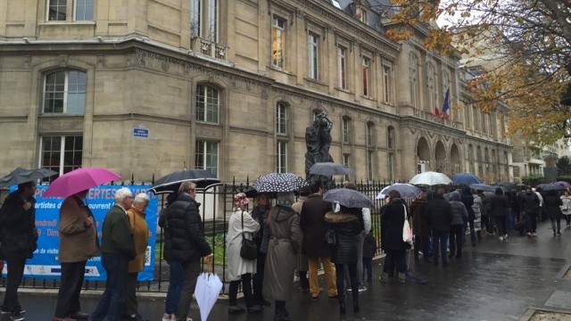 Menschen stehen mit Regenschirmen vor einem Rathaus in Paris