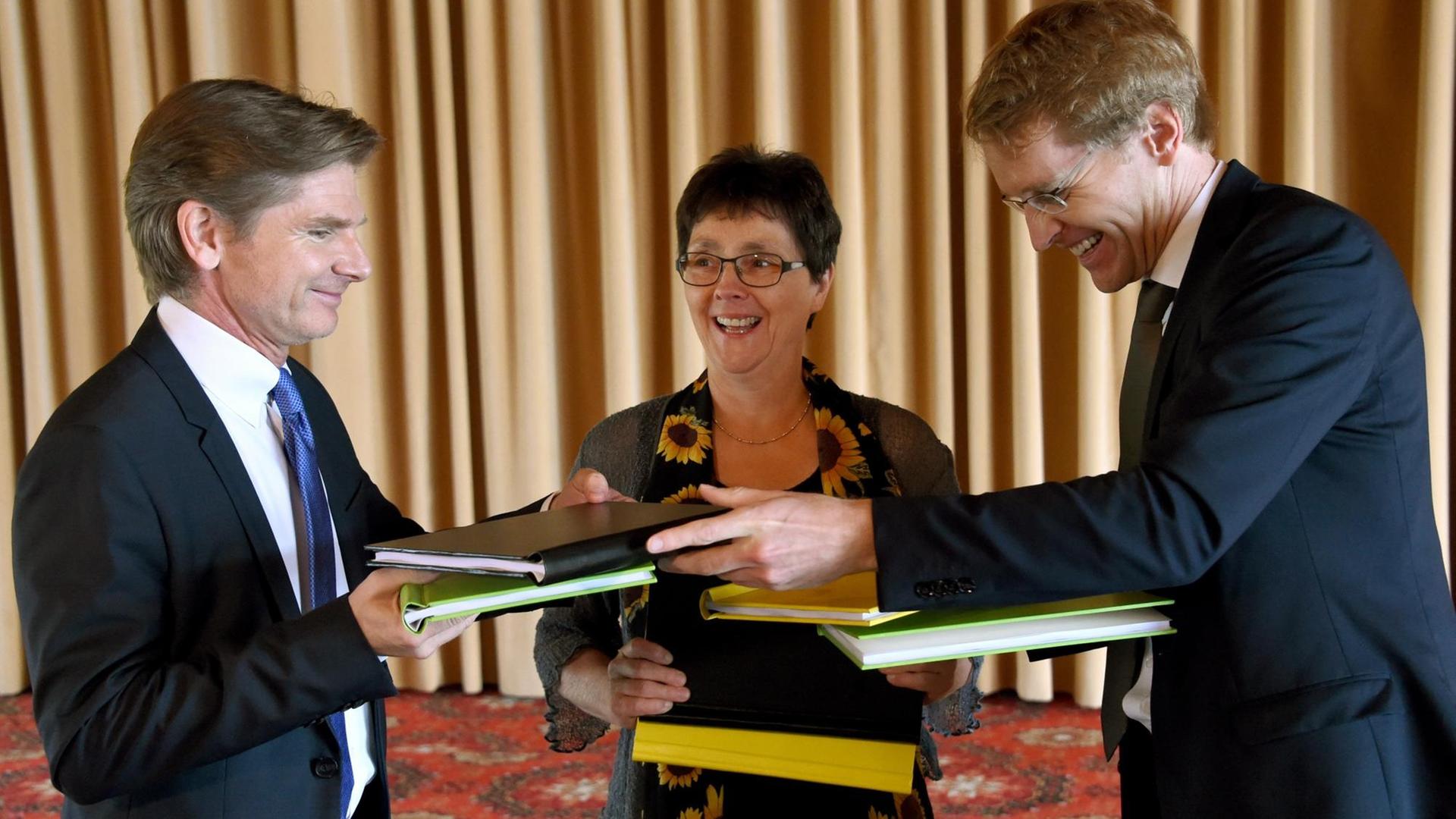 Die Verhandlungsführer der schleswig-holsteinischen Koalitionsverhandlungen, (l-r) Heiner Garg (FDP), Monika Heinold (Bündnis 90/Die Grünen) und Daniel Günther (CDU), hantieren am 16.06.2017 in Kiel (Schleswig-Holstein) mit den Koalitionsverträgen.