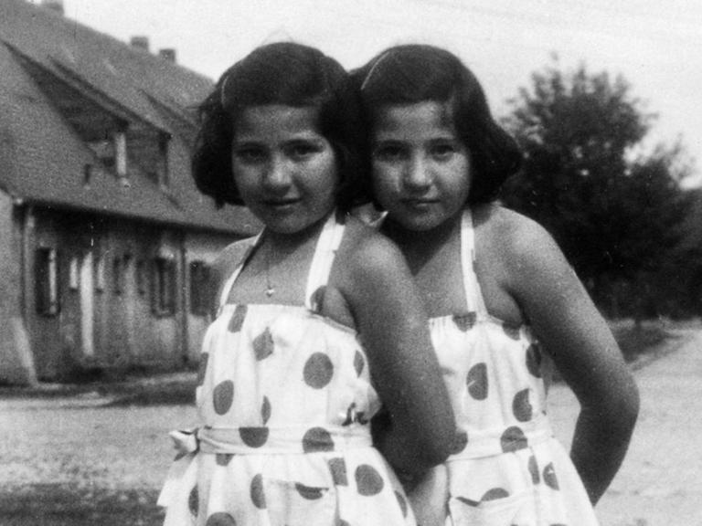 Zwillingsmädchen mit gepunkteten Sommerkleidern stehen auf eine der Straßenzüge in Föhrenwald.