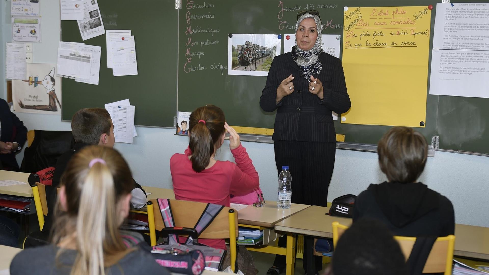 Eine Frau mit Kopftuch steht vor einer Schulklasse und spricht.