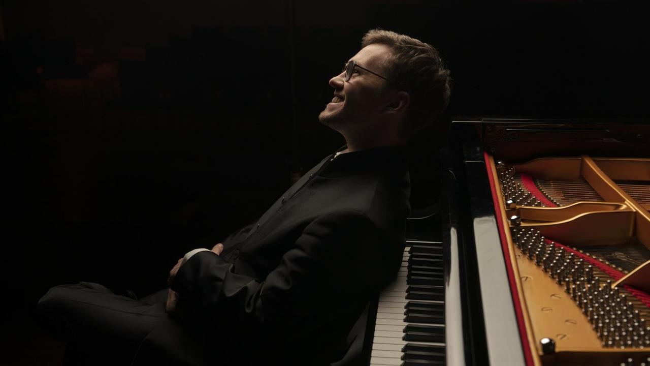 Der Pianist sitzt mit dem Rücken zum Flügel und leht sich lächelnd an die Tasten.