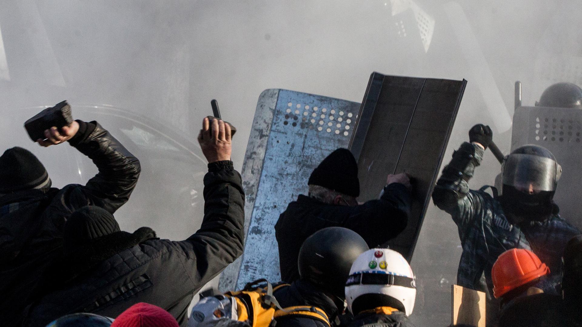 Steinewerfende Demonstranten stehen sich mit Polizisten gegenüber.