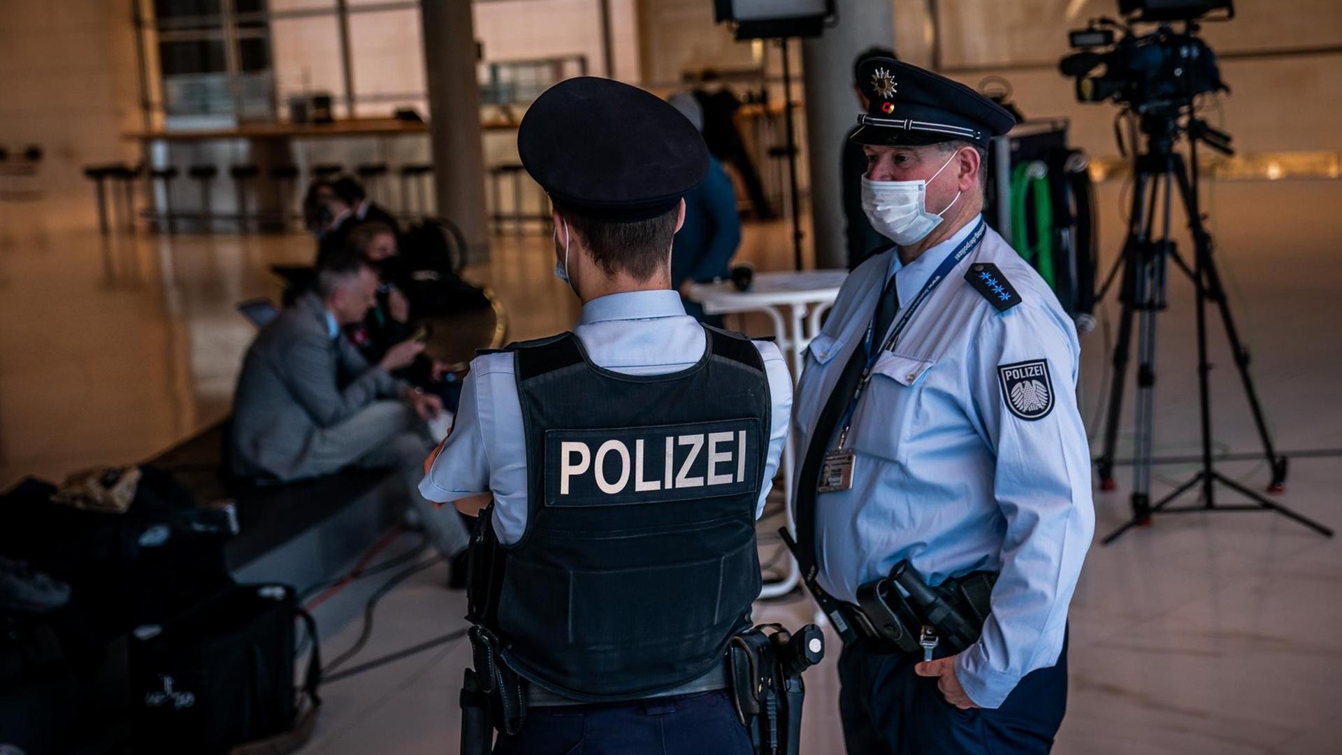 Die beiden Polizisten unterhalten sich, im Hintergrund sieht man Journalisten und Kameras.