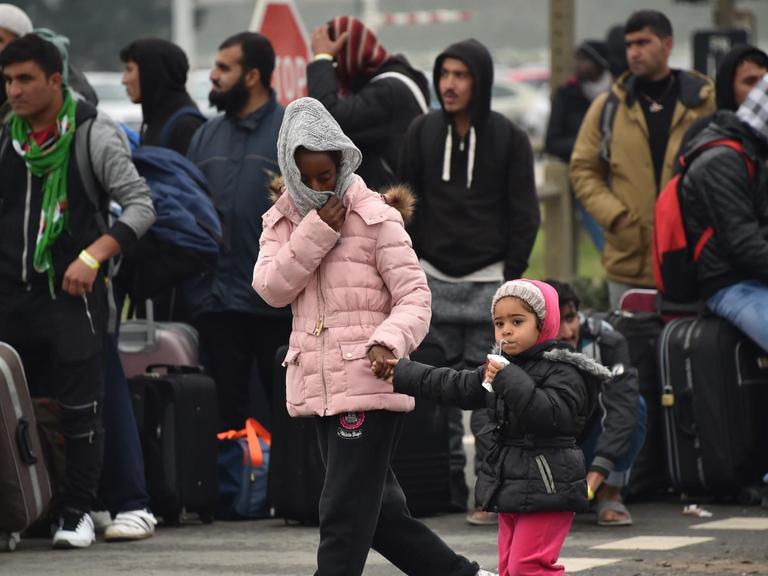 Flüchtlinge warten mit ihrem Gepäck darauf, vom illegalen Lager in Calais in Aufnahmezentren in ganz Frankreich gebracht zu werden.
