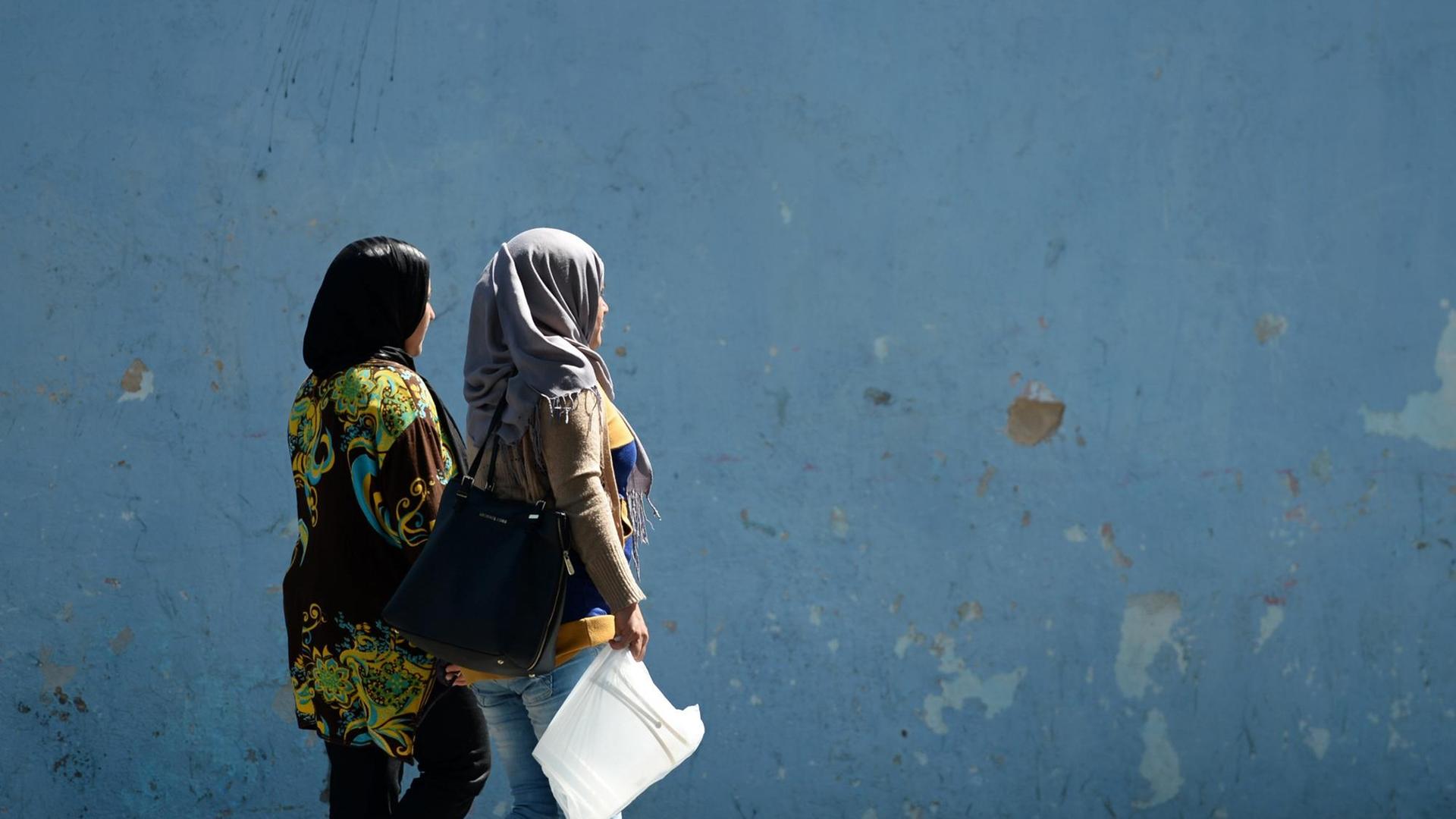 Zwei Frauen gehen in Tunis an einer blauen Wand vorbei